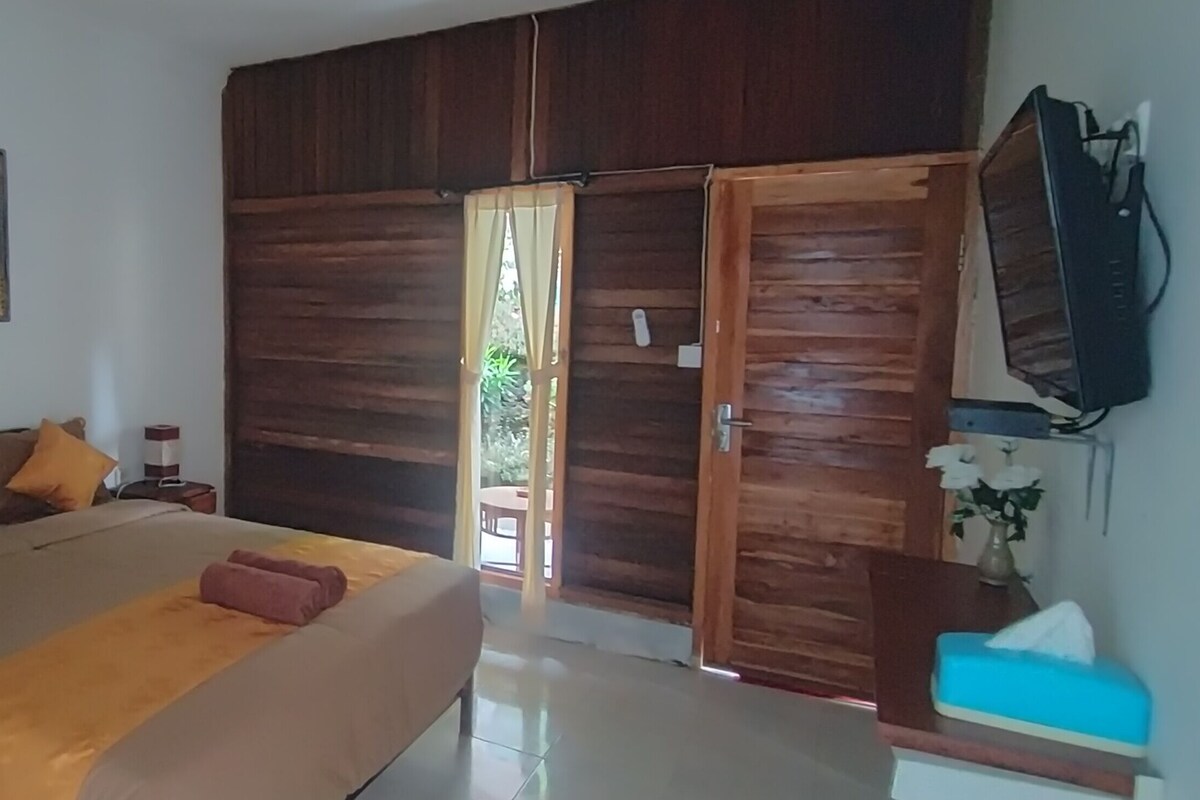 A bedroom with a bed, wooden wardrobe, a television, and a painting on the wall.