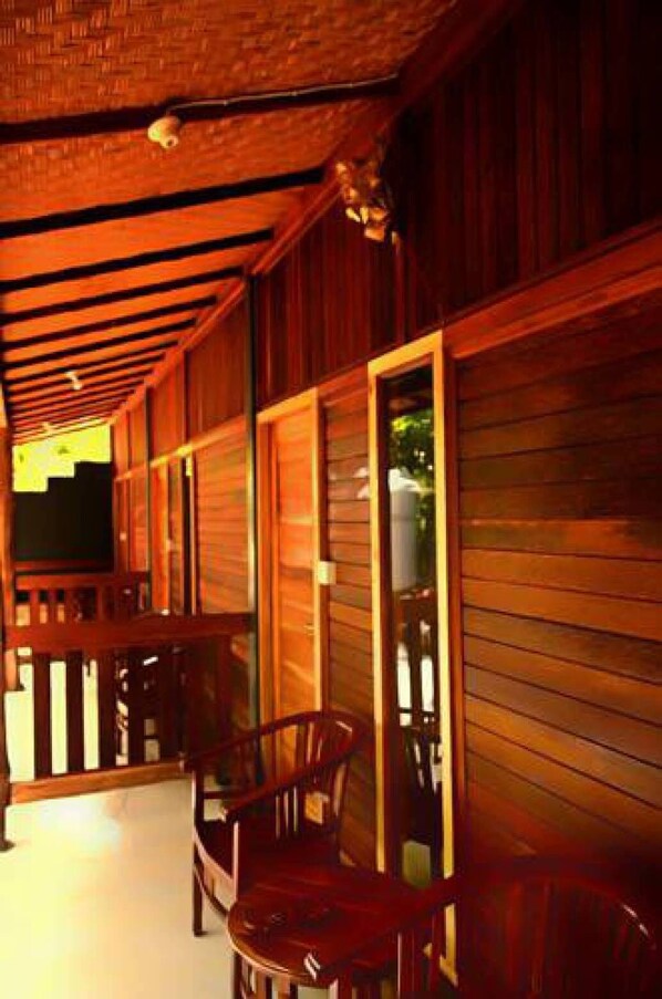 A covered porch with wooden walls and a brick ceiling. There are two wooden chairs and a television mounted on the wall. - The Rahayu Cottage (Penida Island)