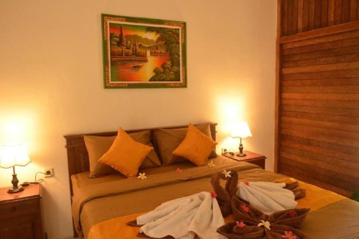 A hotel room with a bed, two nightstands, a wall-mounted painting, and a wooden panel wall.