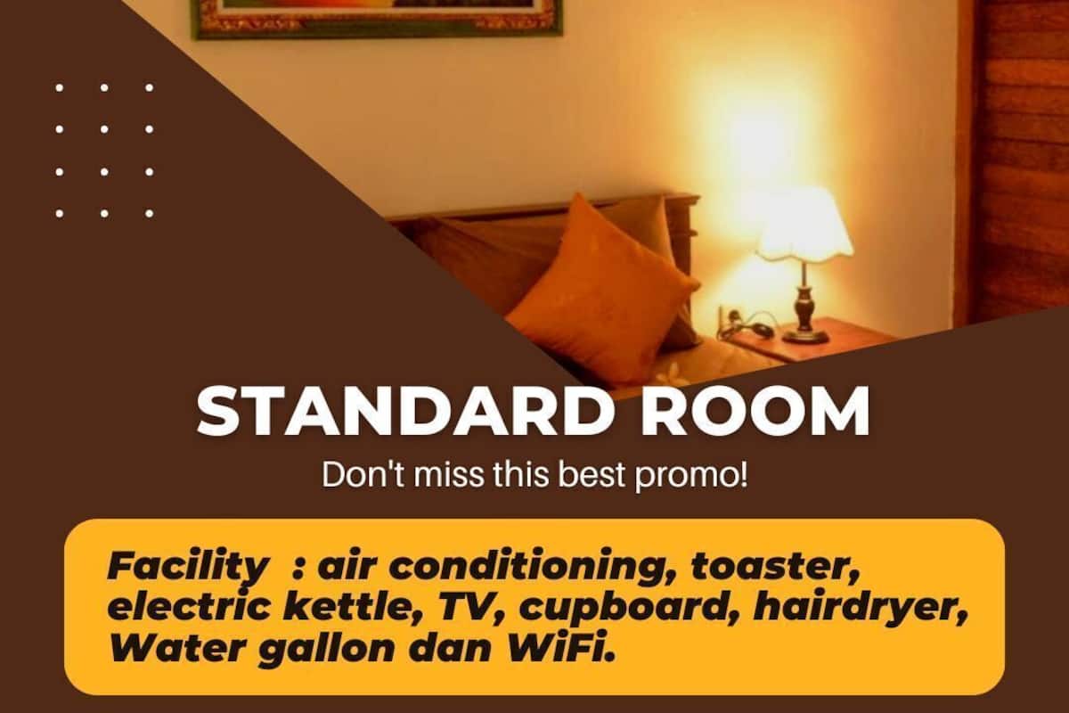 A standard room with a bed, a nightstand with a lamp, a framed picture on the wall, and a list of amenities including air conditioning, toaster, electric kettle, TV, cupboard, hairdryer, water gallon, and WiFi.