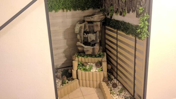 Un pequeño jardín interior con un muro de rocas, un banco de madera y plantas en macetas.