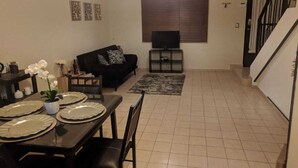 Un comedor con una mesa dispuesta para cuatro personas, un sofá, un televisor y una escalera.