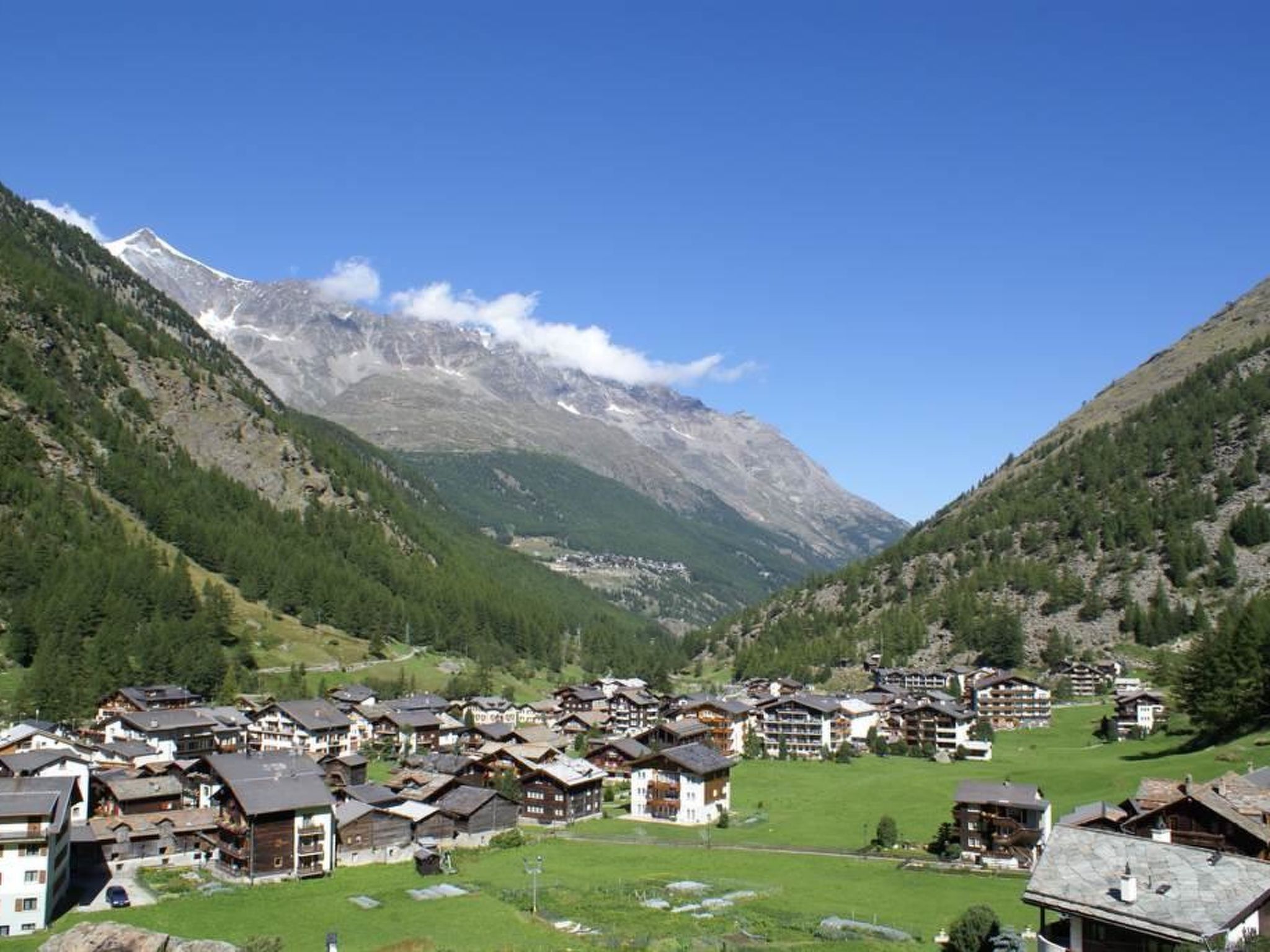 A mountain village with traditional wooden houses, a central square, and a backdrop of snow-capped peaks.