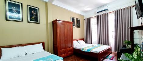 A hotel room with two beds, wooden wardrobe, framed pictures on the wall, curtains, and a potted plant.