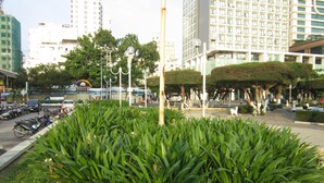 A city square with a central garden, surrounded by modern buildings and parked vehicles. - Forget Me Not Hotel Nha Trang (Nha Trang)