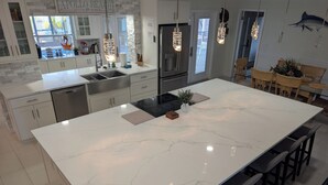A modern kitchen with a large island, white marble countertop, stainless steel appliances, and pendant lights. - Luxury Palm Tree Two / 3 KING BEDS, Put Put golf, HEATED pool, 7 person hot tub (Apollo Beach)