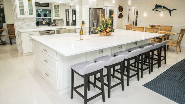 A modern kitchen with a large island, bar stools, and a dining area with wooden chairs. - Luxury Palm Tree Two / 3 KING BEDS, Put Put golf, HEATED pool, 7 person hot tub (Apollo Beach)