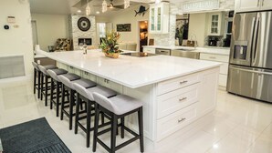 A modern kitchen with a large island, bar stools, and stainless steel appliances. - Luxury Palm Tree Two / 3 KING BEDS, Put Put golf, HEATED pool, 7 person hot tub (Apollo Beach)