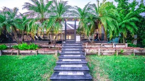 A pathway leading to a building with a glass entrance, surrounded by palm trees and wooden planters. - Luxury Palm Tree Two / 3 KING BEDS, Put Put golf, HEATED pool, 7 person hot tub (Apollo Beach)