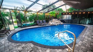 An indoor swimming pool with a clear blue water, surrounded by a brick floor and a glass enclosure. - Luxury Palm Tree Two / 3 KING BEDS, Put Put golf, HEATED pool, 7 person hot tub (Apollo Beach)