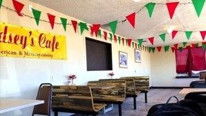 A cafe interior with wooden benches, a yellow sign advertising American & Mexican cuisine, and red and green triangular flags. - Sands Motel (Van Horn)
