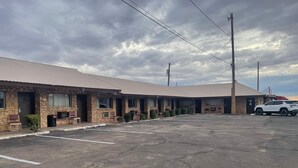 A motel with a row of rooms, a parking lot, and a white SUV parked in the lot. - Sands Motel (Van Horn)