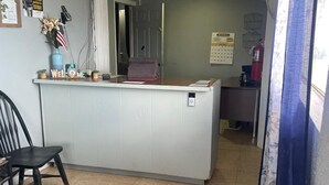 A reception area with a counter, a chair, and a calendar on the wall. - Sands Motel (Van Horn)