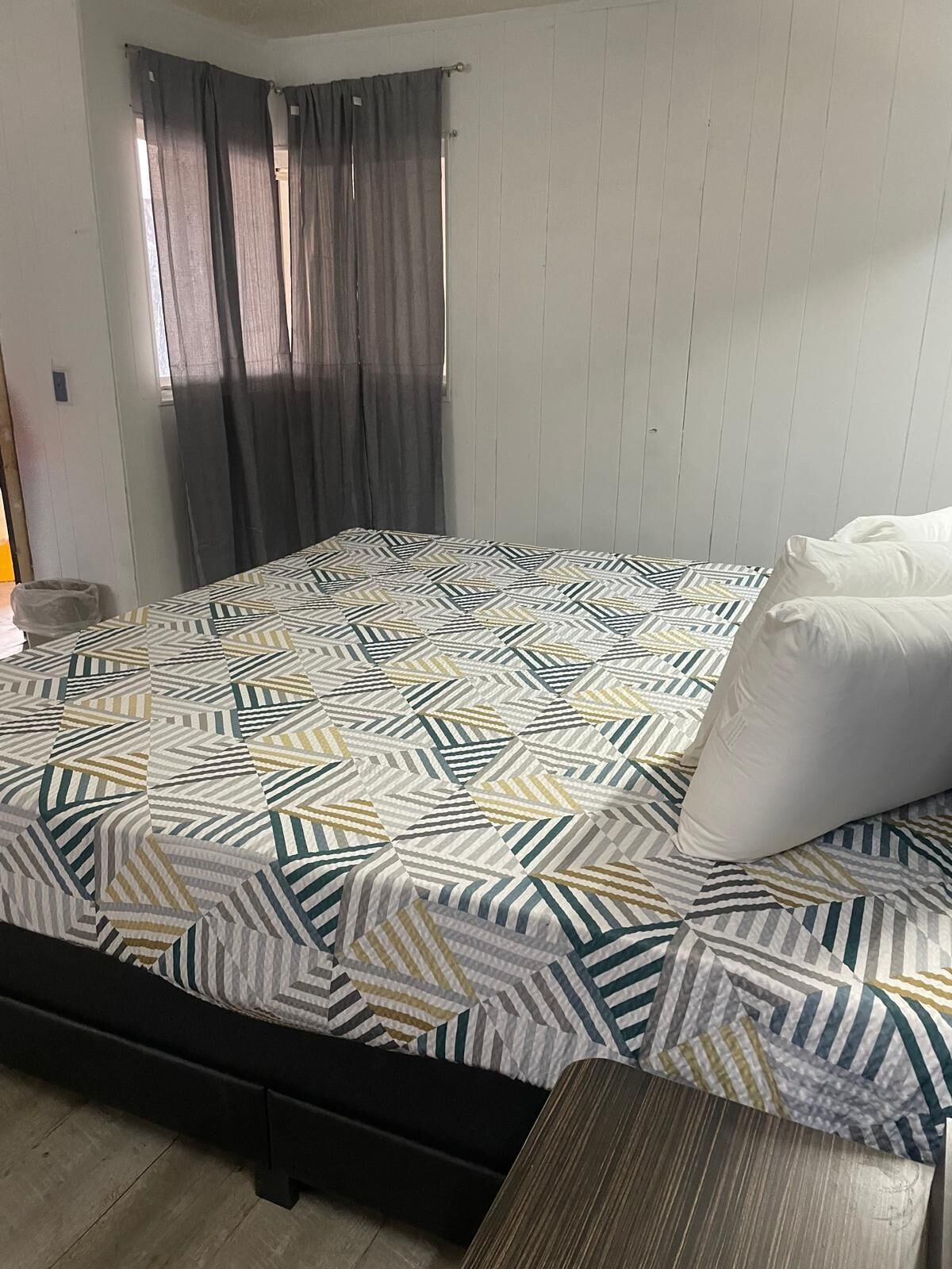 A bedroom with a patterned bedspread, a wooden floor, and a window with curtains.