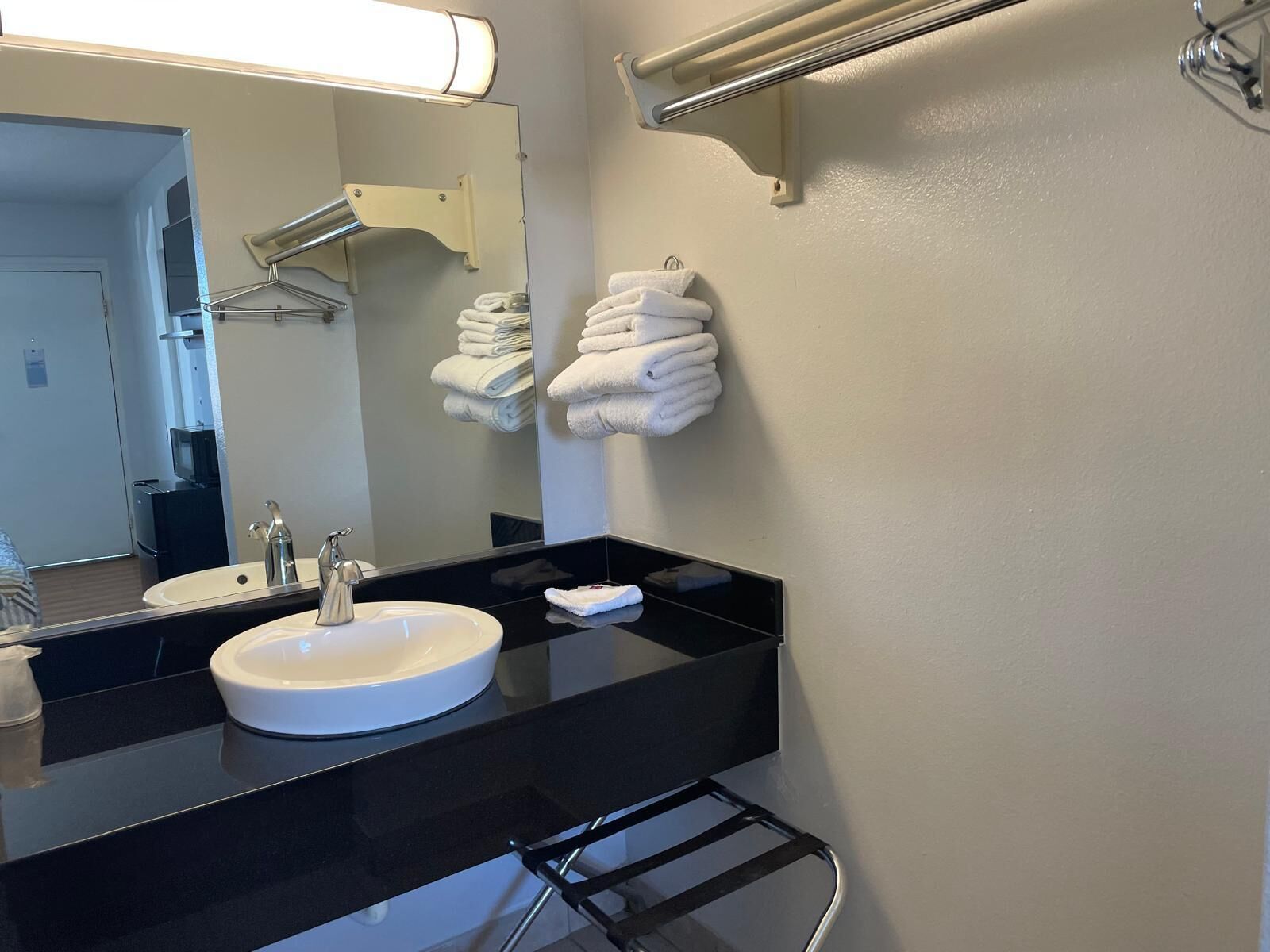 A modern bathroom with a black countertop, white sink, and a large mirror. There are towels hanging on a rack and a towel warmer.