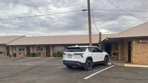 A white SUV parked in a motel parking lot with a brick building and a sign that reads "OFFICE". - Sands Motel (Van Horn)