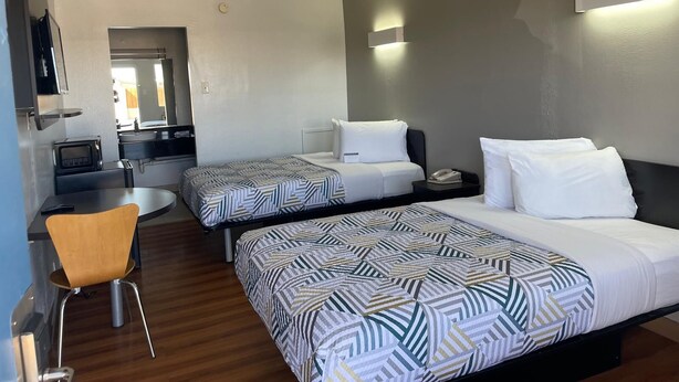 A hotel room with two beds, a small desk, a chair, a TV, and a kitchenette. - Sands Motel (Van Horn)