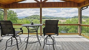 A covered outdoor deck with two chairs and a table, overlooking a scenic landscape. - Ruth's Retreat on South Holston River  (Bristol)