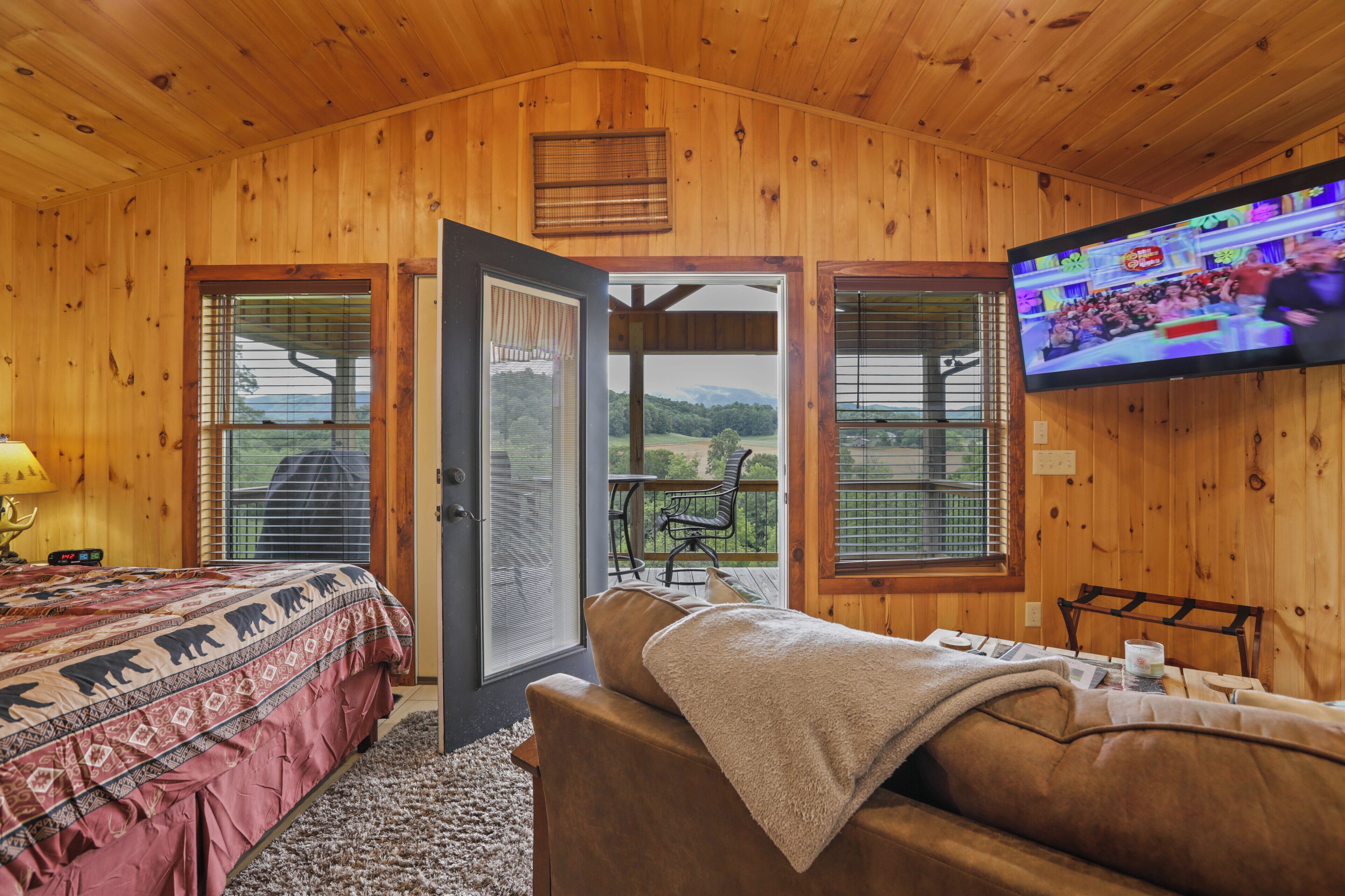 A wooden cabin room with a bed, a sofa, a TV, and a balcony with a table and chairs.