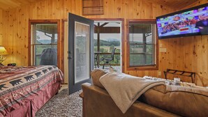 A wooden cabin room with a bed, a sofa, a TV, and a balcony with a table and chairs. - Ruth's Retreat on South Holston River  (Bristol)