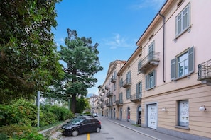 Una calle con autos estacionados, un edificio con balcones y vegetación.