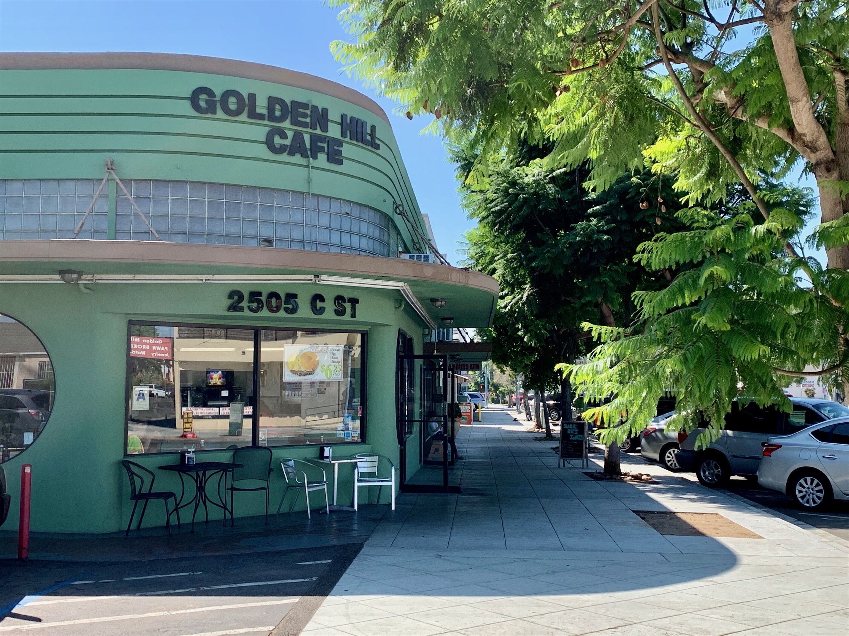A vintage-style cafe with a green facade, outdoor seating, and a clear view of the street.