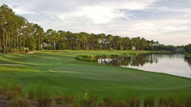 A golf course with a pond, surrounded by trees and a clear sky.