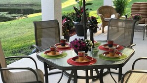 An outdoor patio with a table set for four, surrounded by wicker chairs, with a view of a pond and a deer in the background.