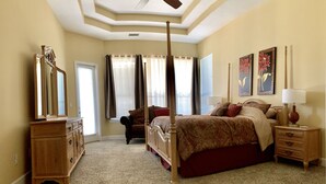 A bedroom with a large bed, a dresser, a nightstand, a ceiling fan, and two wall-mounted lamps.