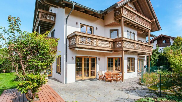 Une maison à deux étages avec un balcon, une terrasse en pierre et un petit jardin.