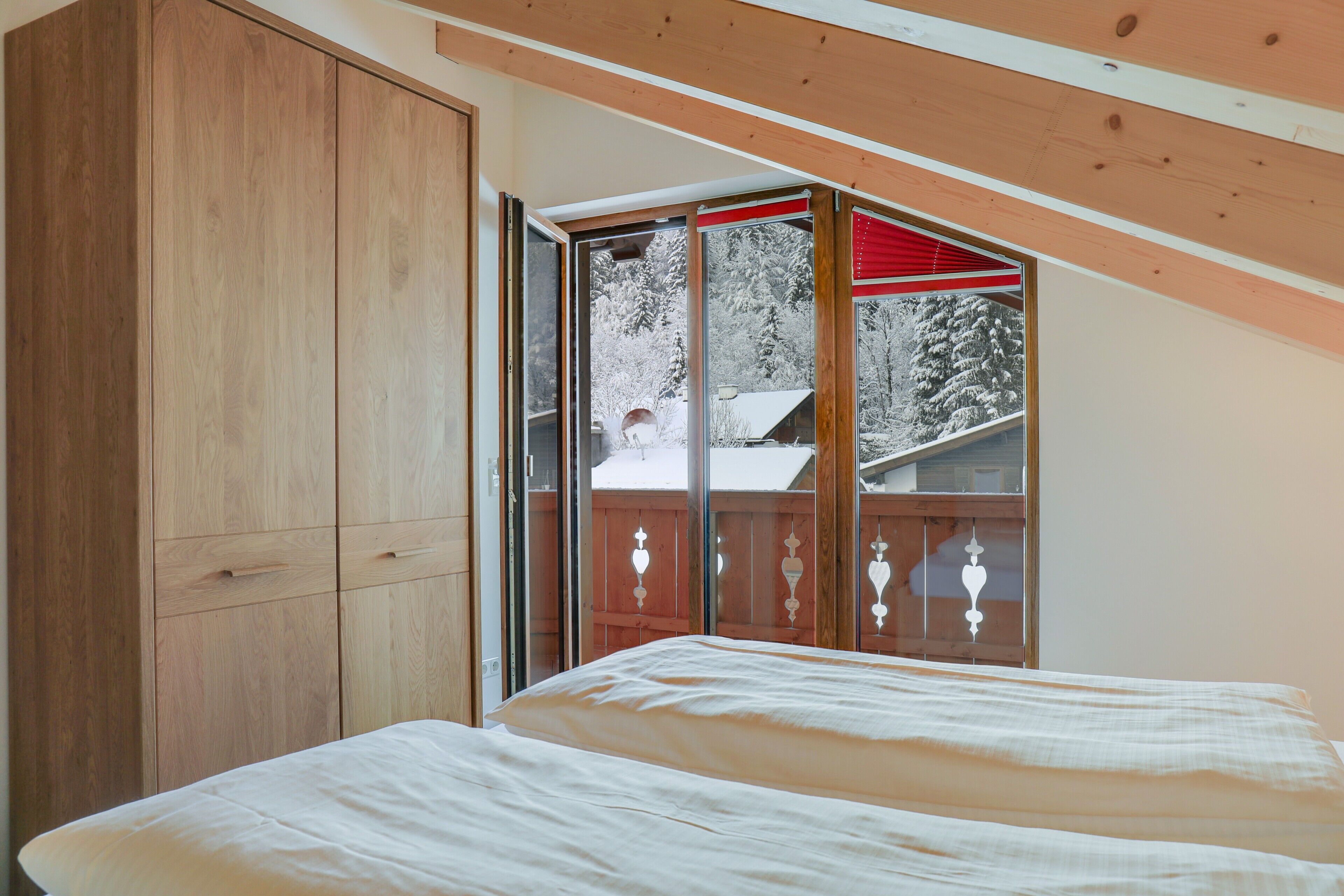 Camera da letto con un letto, un'armadio in legno e una porta scorrevole in vetro che dà su un balcone con vista sugli alberi.