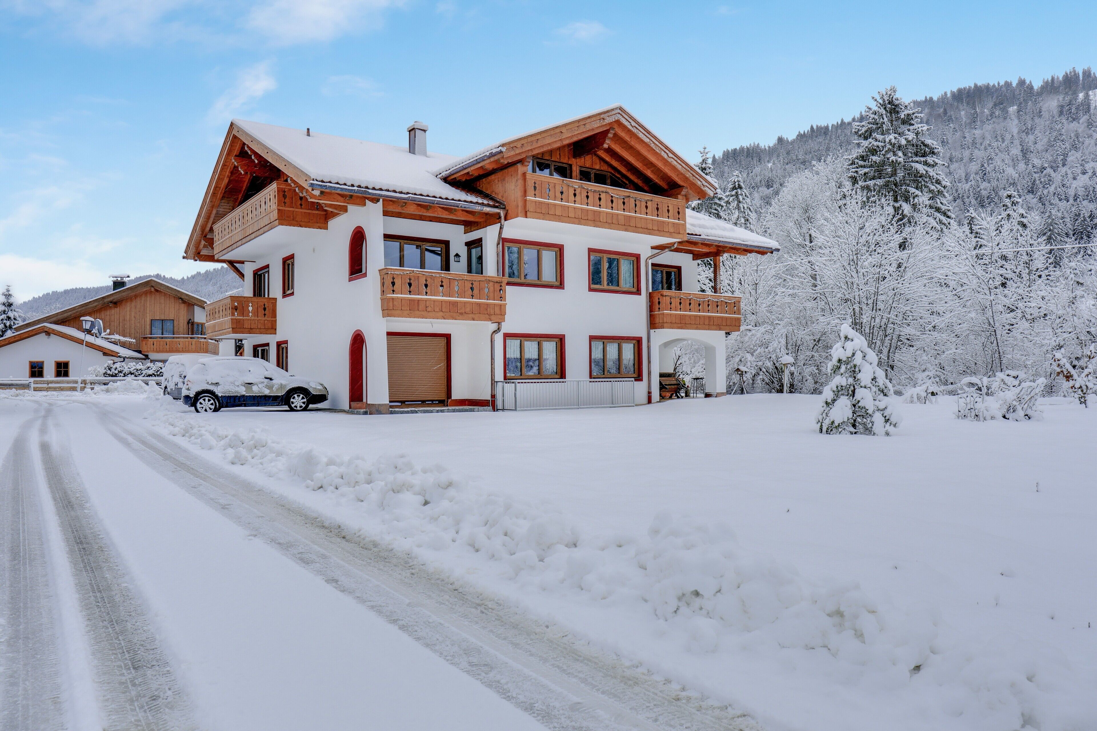 Un chalet de varios pisos con un camino cubierto de nieve y vista a una montaña boscosa.