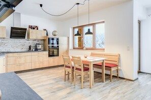 A modern kitchen with wooden cabinets, a stone backsplash, and a dining area with a bench and chairs. - Beautiful Holiday Apartment "Geroldsee" with Mountain View & Balcony (Garmisch-Partenkirchen)