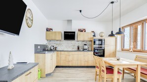 Een moderne keuken met houten kastjes, een betegelde muur, een eethoek met een tafel en stoelen, en een groot raam.