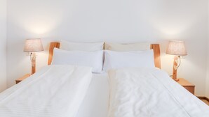 Een tweepersoonsbed met witte lakens, twee bedlampjes en een houten nachtkastje.