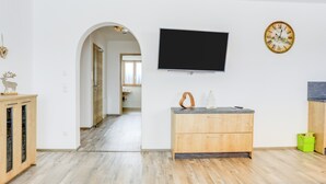 Een moderne woonkamer met een flatscreen televisie, houten kasten en een klok aan de muur.