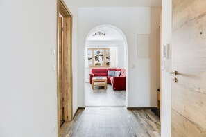 A hallway leading to a living room with a red sofa, wooden flooring, and a view through an arched doorway. - Beautiful Holiday Apartment "Geroldsee" with Mountain View & Balcony (Garmisch-Partenkirchen)
