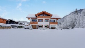Een groot, meerlaags gebouw met een opvallend balkon, omringd door met sneeuw bedekte bomen en een heldere lucht.