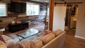 Een moderne woonkamer met een bank, een glazen salontafel en een televisie bevestigd aan een houten wand.