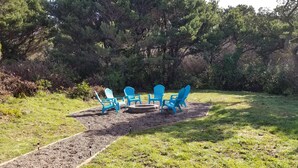 Een tuin met vuurkorf en blauwe Adirondack-stoelen.
