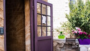 Un bâtiment en pierre avec une porte violette, un sol carrelé et une petite table ornée de plantes en pot.