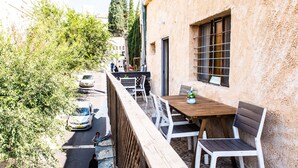 Un petit patio extérieur, avec une table en bois et des chaises blanches, entouré d’un mur de pierre et de verdure.