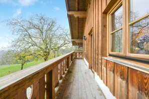 A wooden balcony with a railing, large windows, and a view of trees and a grassy field. - Holiday Apartment "Morgenrot" with Mountain View, Balcony & Garden (Wackersberg)