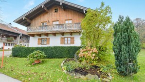 Una casa de madera tradicional con balcón, rodeada por un jardín bien cuidado con diversas plantas y setos.