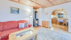 Una sala de estar con sofá, una mesa de centro de vidrio, chimenea y una cocina visible a través de un arco.