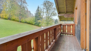 A wooden deck with a railing, a covered porch, and a view of a green lawn and trees. - Holiday Apartment "Sommerwind" with Mountain View, Garden & Balcony (Wackersberg)