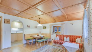 A cozy living room with a wooden ceiling, a dining area with a bench, a sofa with patterned cushions, and a kitchen visible through an archway. - Holiday Apartment "Sommerwind" with Mountain View, Garden & Balcony (Wackersberg)