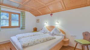 A wooden ceiling, a bed with floral bedding, a nightstand, a chair, and a window with curtains. - Holiday Apartment "Sommerwind" with Mountain View, Garden & Balcony (Wackersberg)