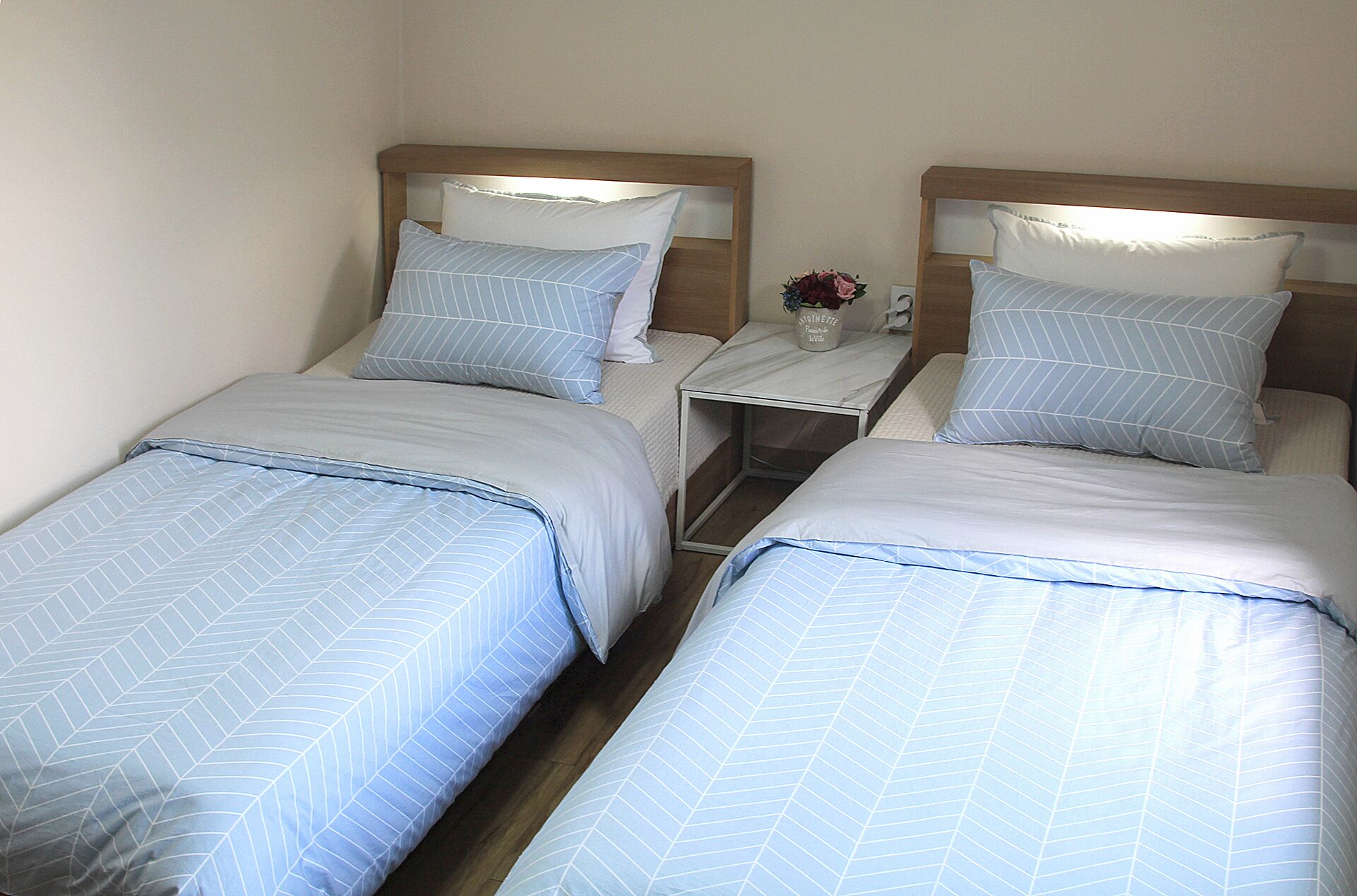 Two single beds with matching headboards and pillows, a small bedside table with a vase of flowers, and a nightstand with a lamp.