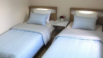 Two single beds with matching headboards and pillows, a small bedside table with a vase of flowers, and a nightstand with a lamp.